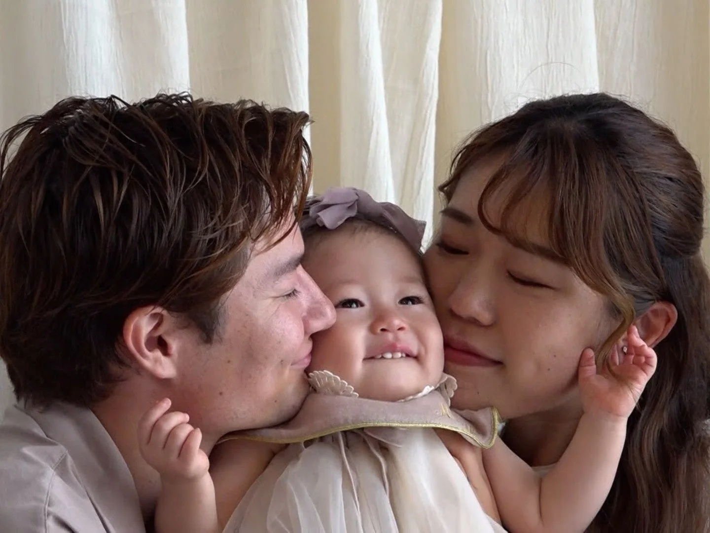 両親が赤ちゃんにキスをして愛情を表現している、幸せそうな家族のポートレートです。赤ちゃんは笑顔で、温かい絆が感じられます。