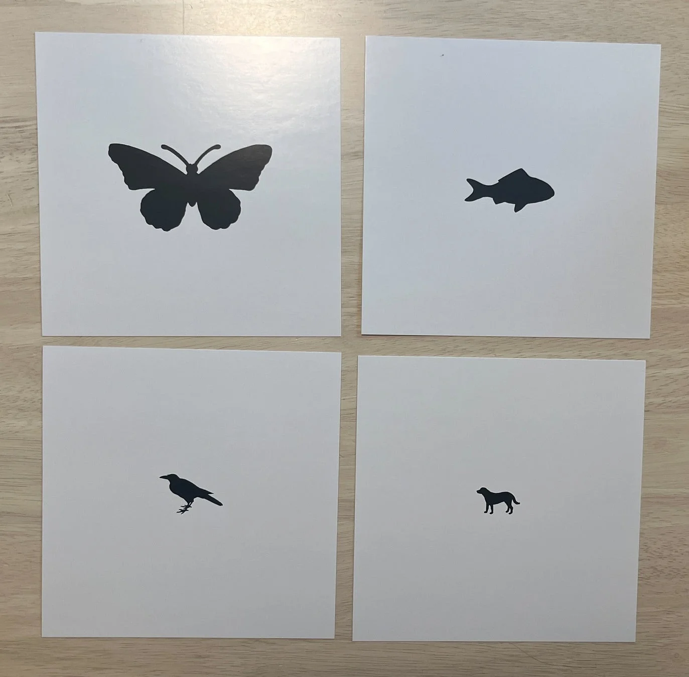 白いカードに蝶、魚、カラス、犬のシルエットがそれぞれ描かれ、2x2のグリッド状に配置されています。シンプルでミニマルな動物のイラストです。