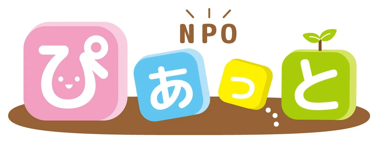 「NPOぴあっと」という文字が、それぞれピンク、水色、黄色、緑色の可愛らしいブロック状の文字で表現されています。緑のブロックには小さな双葉が生えており、親しみやすく、成長やコミュニティを連想させるイラストです。
