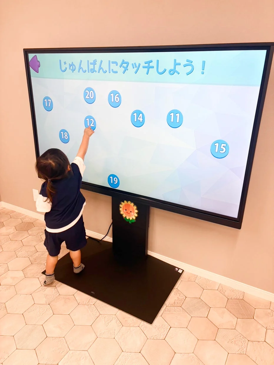 大型タッチスクリーンで知育ゲームをする幼児