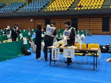体育館のような会場でゼッケンの準備をするスタッフ