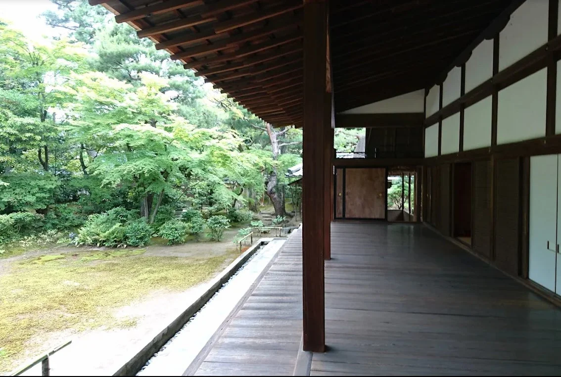 伝統的な日本家屋の縁側から、手入れの行き届いた美しい日本庭園を眺める風景。豊かな緑の木々や苔が広がり、静かで落ち着いた雰囲気が感じられます。