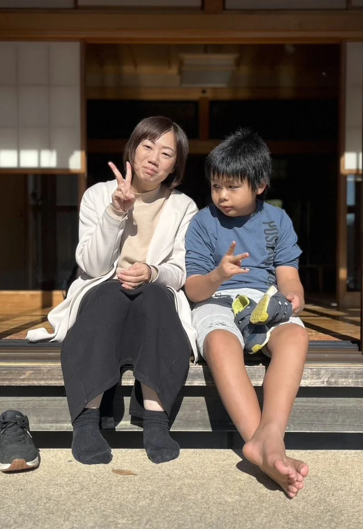 晴れた日に日本家屋の縁側に座る女性と男の子の親子。二人はピースサインをしており、リラックスした和やかな雰囲気が感じられます。男の子は靴を抱えています。