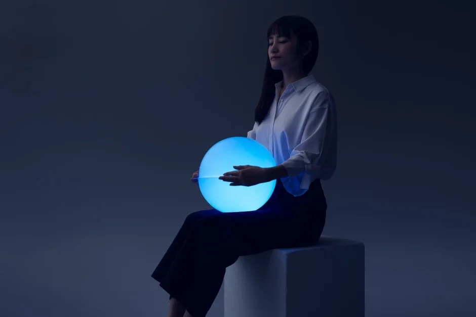 暗い空間で、女性が目を閉じて青く光る球体を両手で抱えている