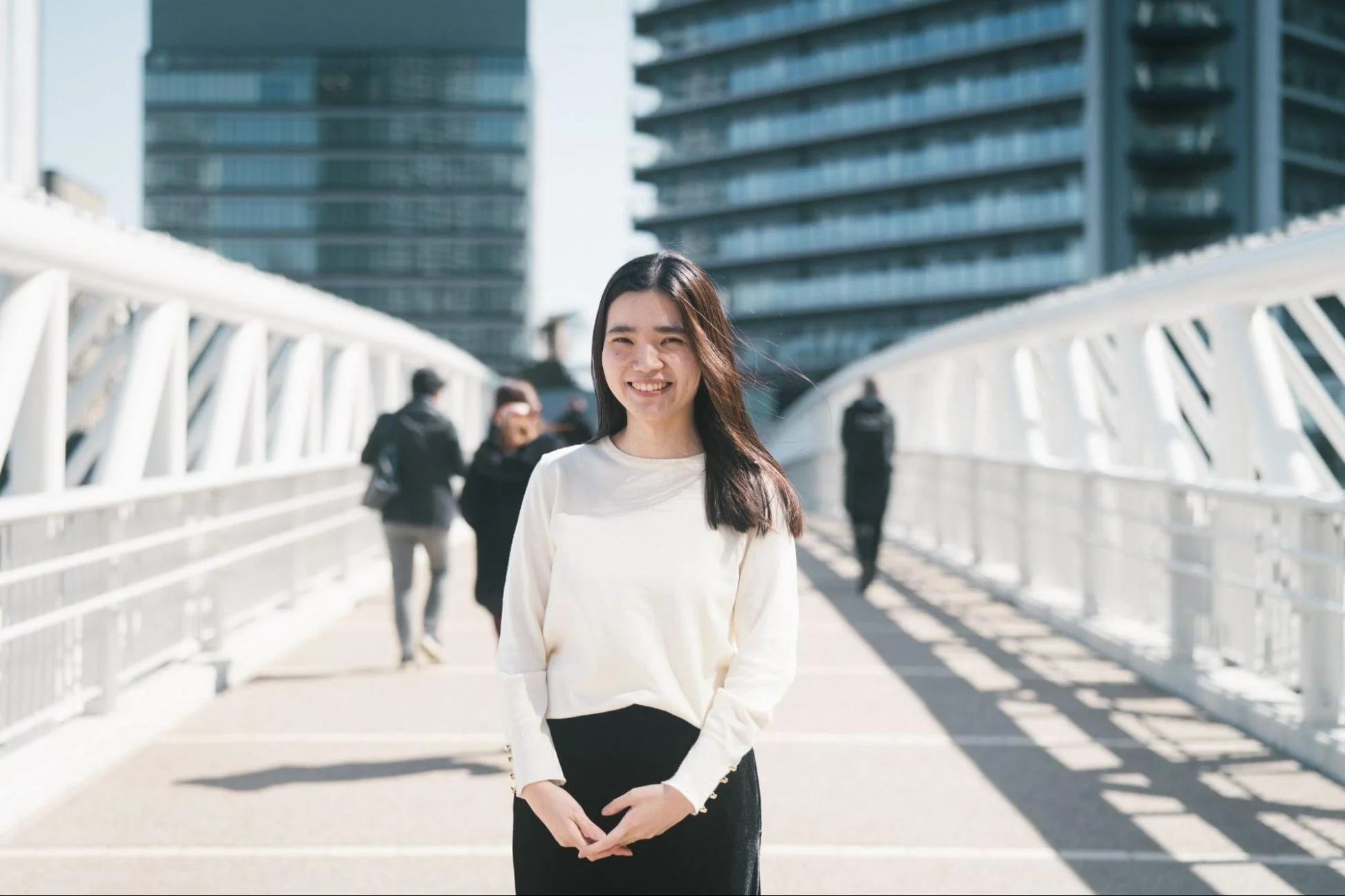 都市の歩道橋の上で笑顔で立つ若いアジア人女性のポートレート。