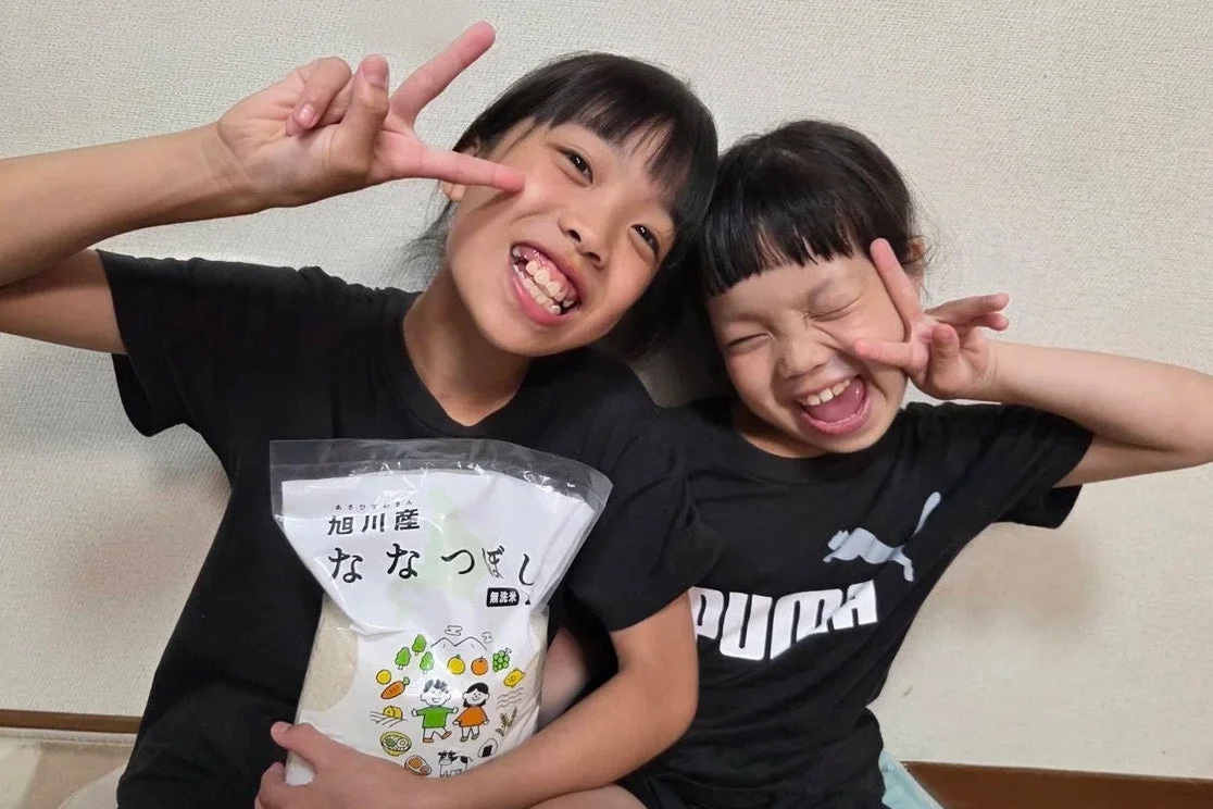 お米の袋を持ってピースサインをする子どもたち