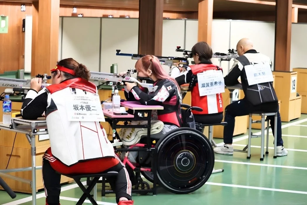 屋内の射撃場で、車椅子を使用するアスリートがライフルを構え、ターゲットを狙っている様子