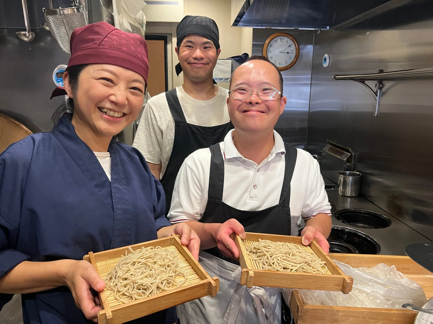 厨房で笑顔で並び、そばを持つ人々