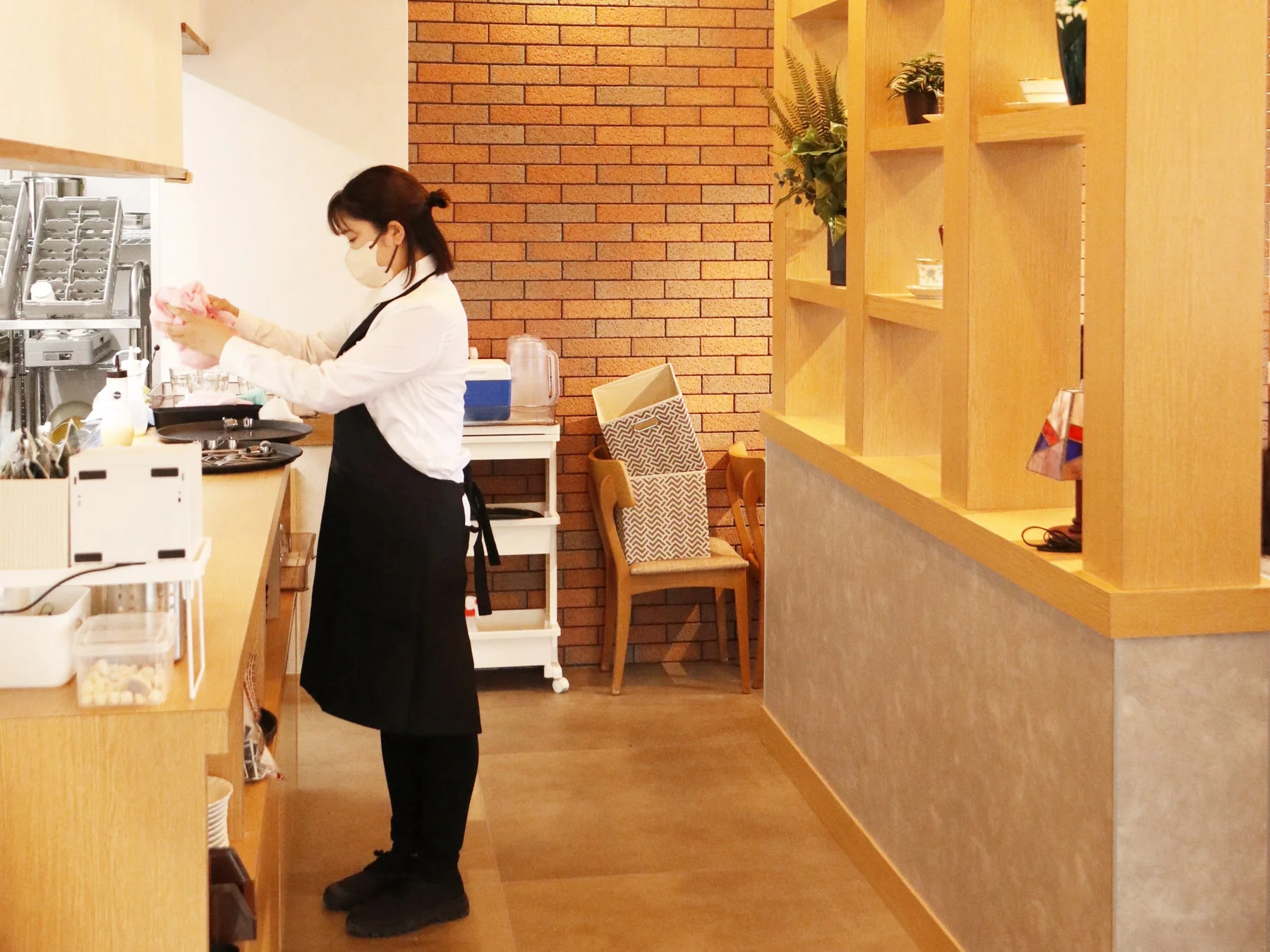 マスクとエプロンを着用した女性店員がカフェのカウンターで作業している様子