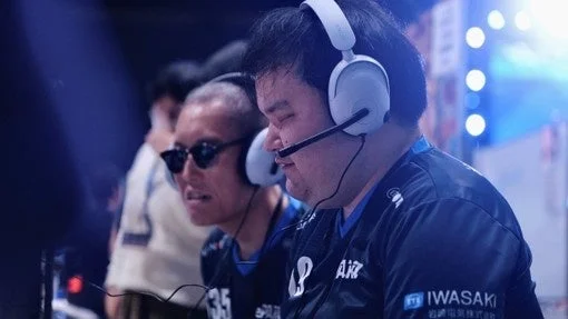 eスポーツの大会やイベントで、ヘッドセットを装着した2人の男性が真剣な表情でゲームに集中している様子。青い光が特徴的な屋内の雰囲気。