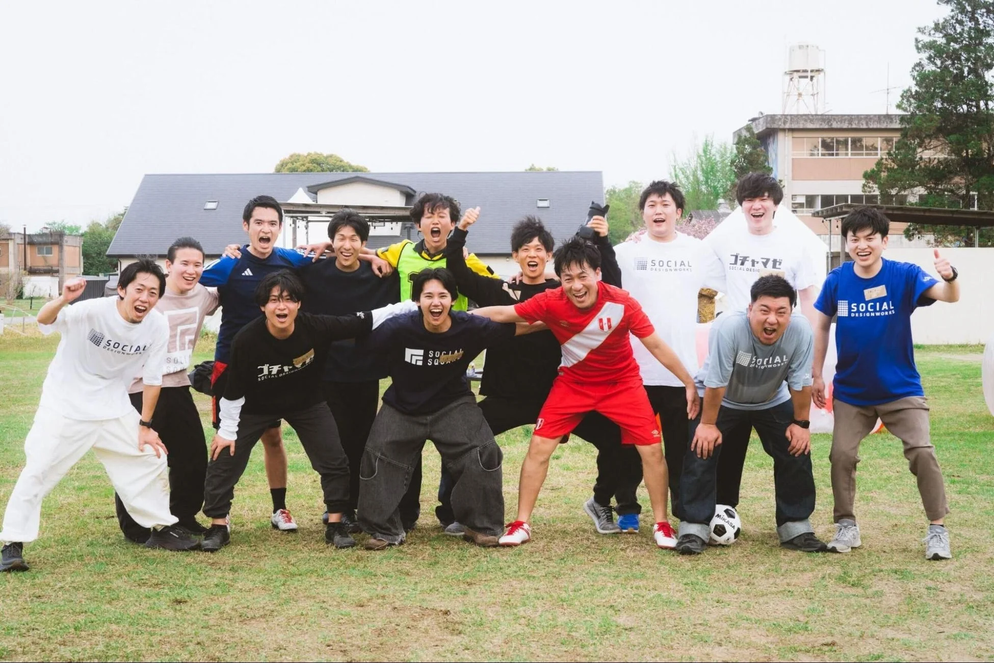 芝生の上で多くの男性が楽しそうにポーズをとっている集合写真