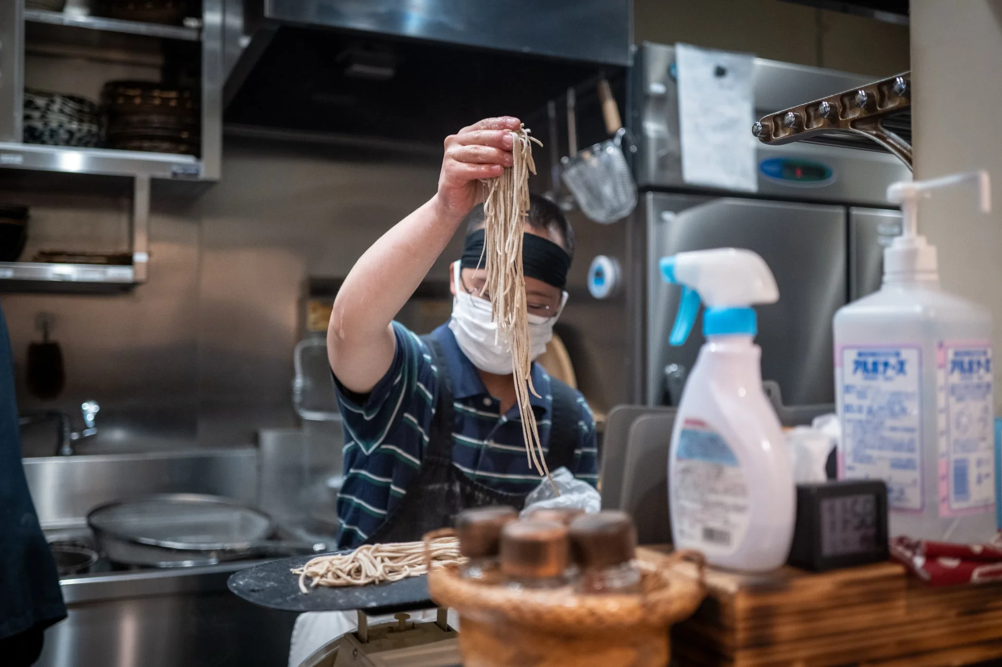 マスクと鉢巻を着用した料理人が麺を調理