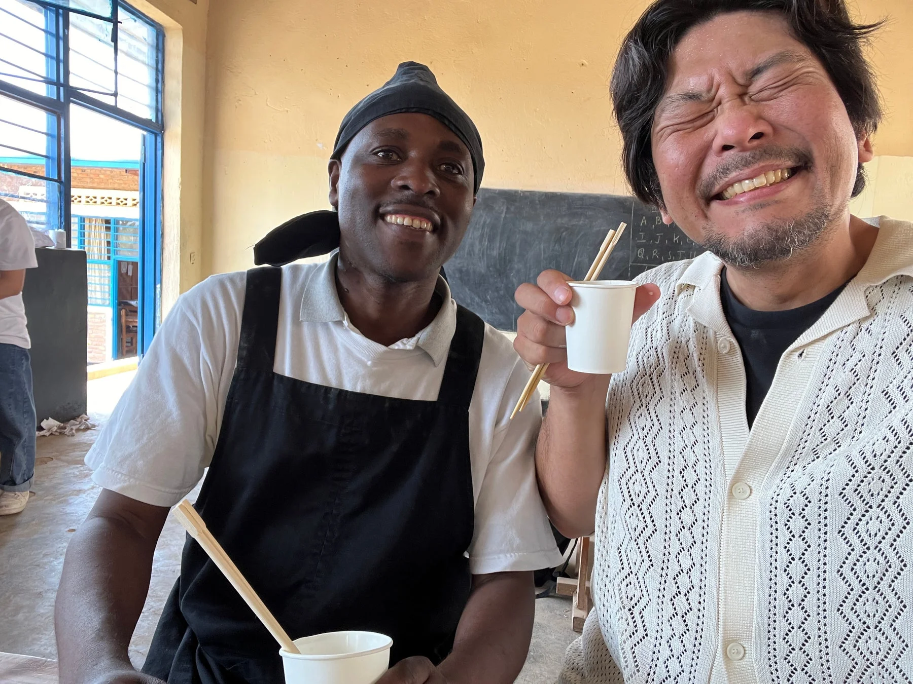 笑顔の男性二人、紙コップと箸を持つ