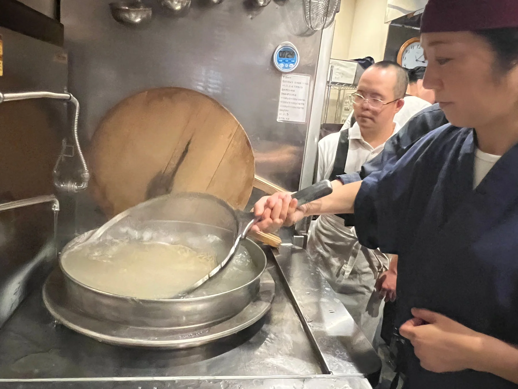 厨房で麺を茹でる調理師と見守るスタッフ