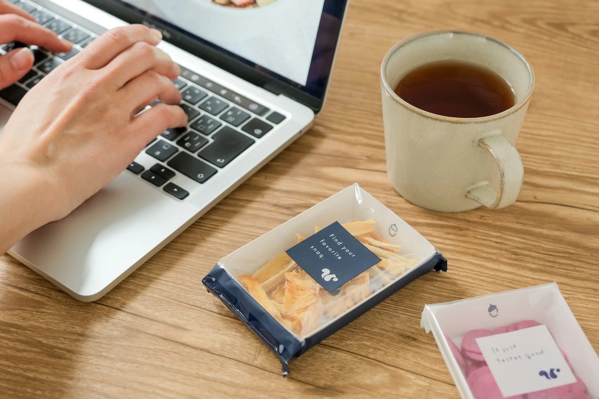木製デスクでノートパソコンとスナック、マグカップ
